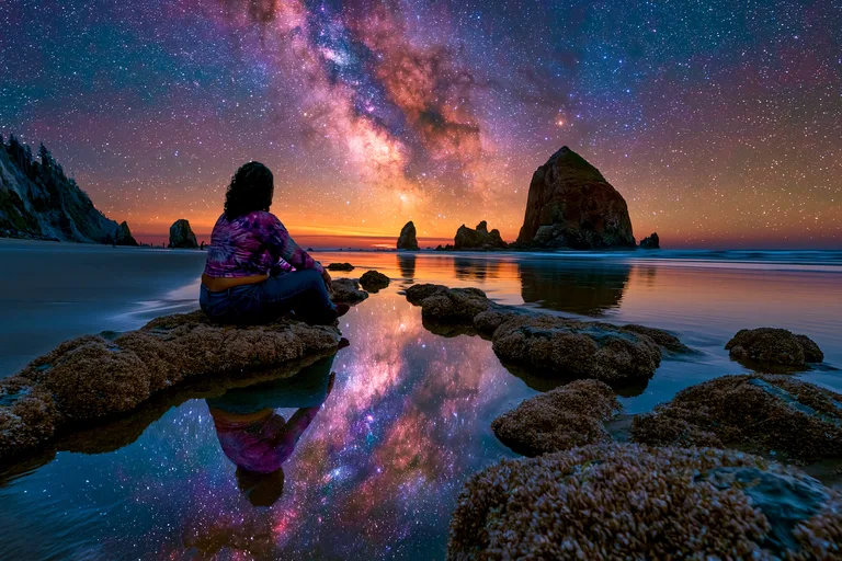 A person sits on a rock at the edge of the ocean, gazing at the