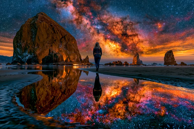 A lone woman stands on a beach, gazing at a vibrant, star-filled sky